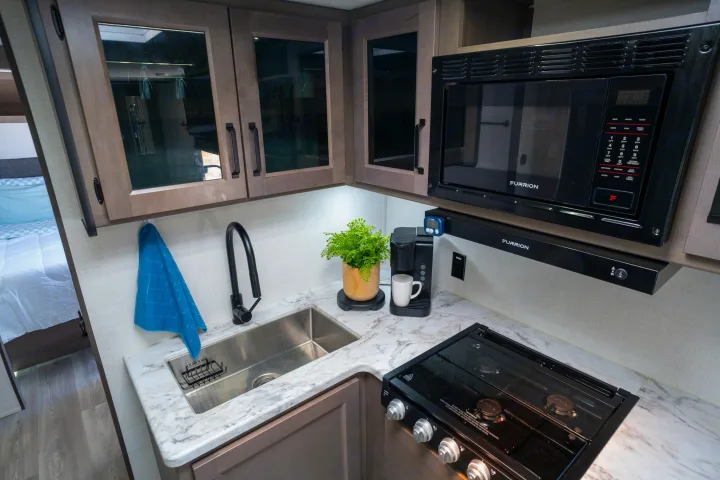 Bright and functional RV rental kitchen with a sink, microwave, stovetop, and coffee maker. Perfect for trips.. Grand Design Transcend Xplor 2024