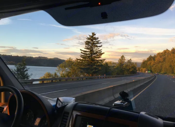 Scenic RV rental journey: driving a highway alongside a wide river. Golden light on trees and distant hills under a vast sky.. Forest River Coachmen Prism 2016