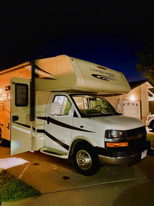 This Class C motorhome, an RV rental option, parked at night on a driveway with its door open, ready for adventure.. Coachmen Leprechaun 2016