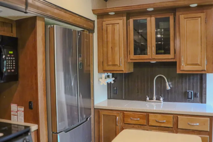Modern RV rental kitchen featuring a stainless steel fridge, sink, wood cabinets, and microwave.. Forest River Coachmen Chaparral 2018