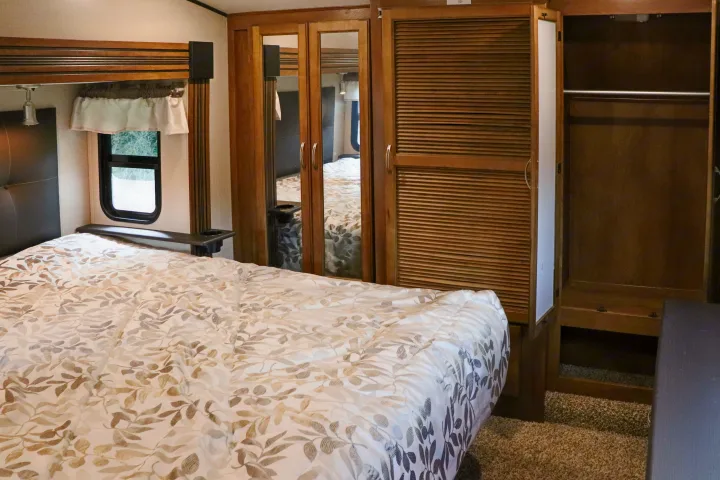 RV rental bedroom with a comfortable bed, leafy comforter, and ample built-in mirrored and louvered closet storage.. Forest River Coachmen Chaparral 2018