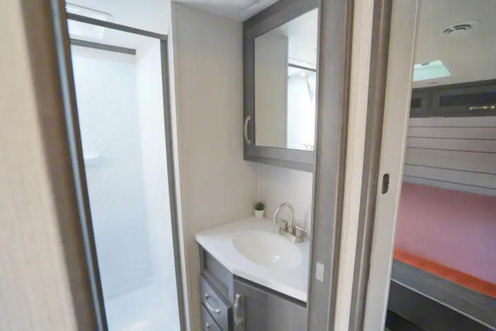 Compact RV rental bathroom: features a modern shower, vanity with sink & mirror, leading to an adjacent bedroom area.. Keystone Cougar 2024