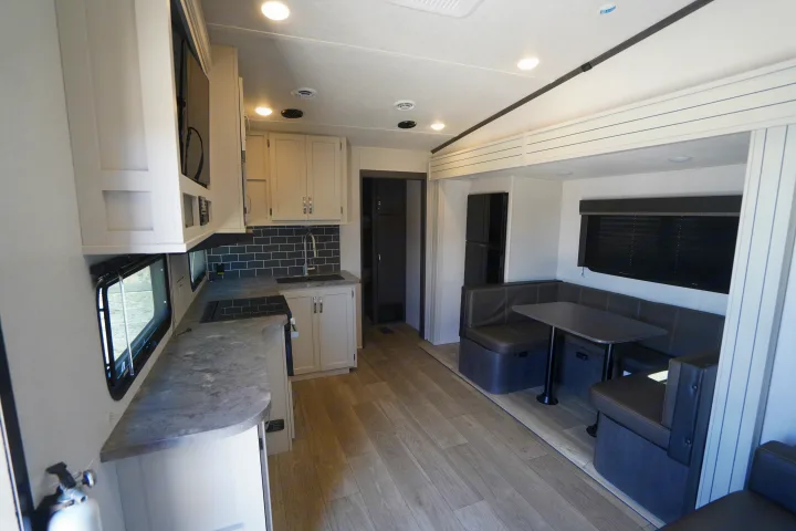 Spacious and modern RV rental interior featuring a full kitchen with black subway tile and a comfortable dining booth.. Keystone Cougar 2024