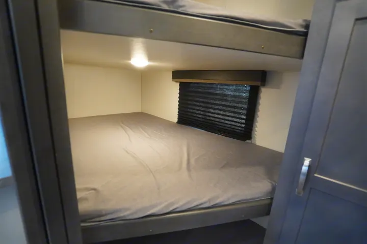 Cozy RV rental bunk beds, perfect for family sleeping. Features a comfortable lower bed, window blind, and interior lighting.. Keystone Cougar 2024