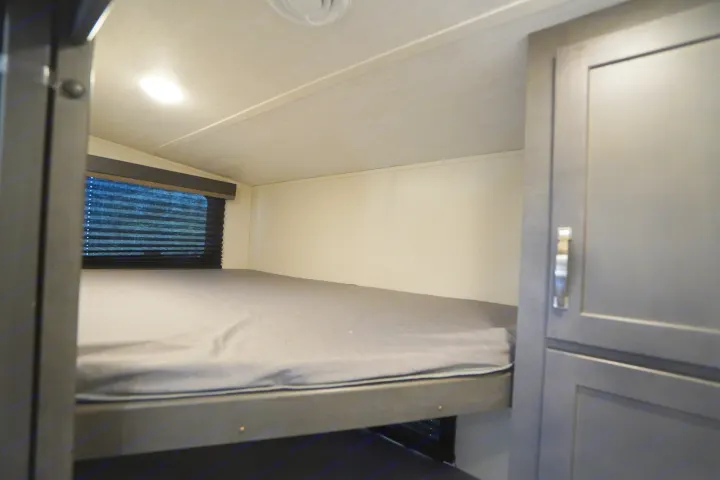 Cozy RV rental bunk bed interior, ideal for families. Features a window with blinds and convenient storage cabinet.. Keystone Cougar 2024