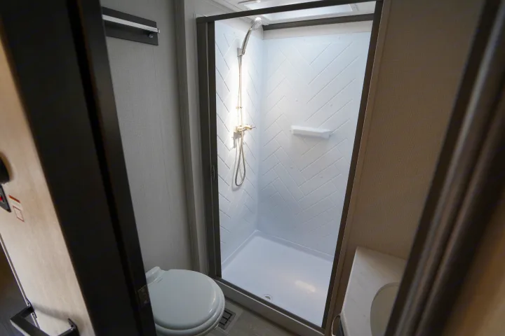 Experience comfort in this RV rental bathroom: features a toilet, shower with herringbone walls, and a vanity.. Keystone Cougar 2024