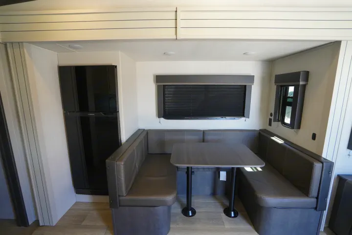 RV rental interior featuring a spacious dinette with gray seating, a table, and a large black refrigerator. Ideal for travel.. Keystone Cougar 2024
