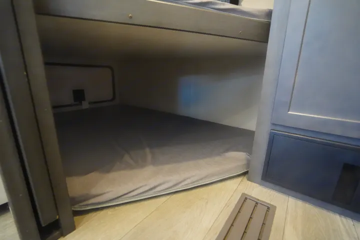 Explore this modern RV rental's interior: a comfortable lower bunk with window, power outlet, and floor vent.. Keystone Cougar 2024