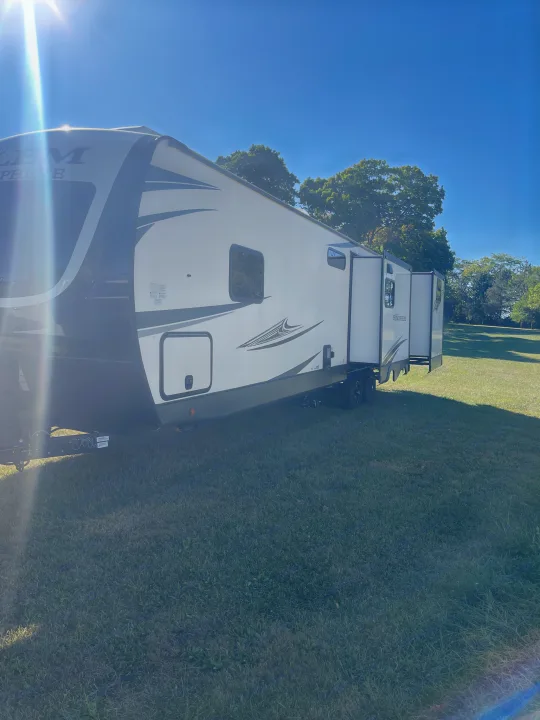 A bright white travel trailer RV rental with slide-outs extended, parked on a sunlit grassy field under a clear blue sky.. Forest River Salem Hemisphere 2020