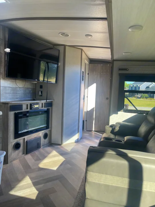 Modern RV rental living space featuring a TV, electric fireplace, and comfortable recliners. Sunlight brightens the interior.. Forest River Salem Hemisphere 2020