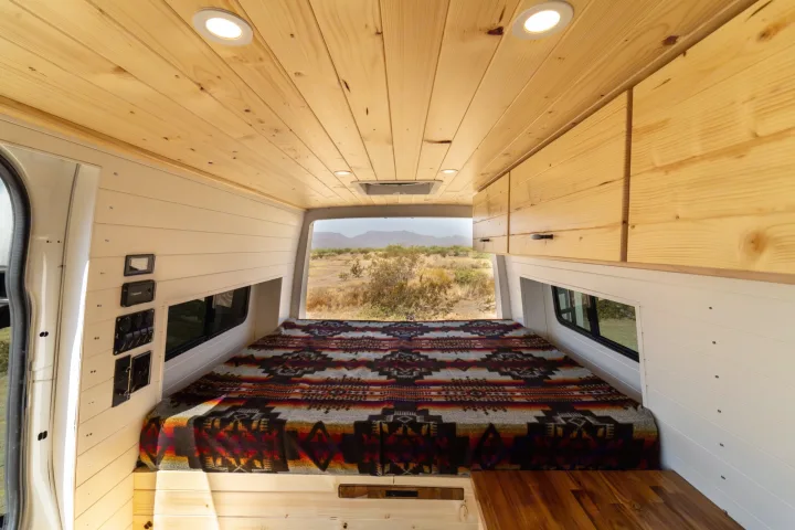 Experience van life: This rv rental shows a cozy camper interior with wooden ceiling, comfortable bed, and a stunning desert view.. Mercedes-Benz Sprinter 2021