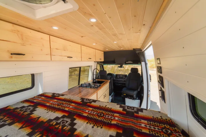Bright and modern rv rental interior featuring custom wood ceilings, overhead cabinets, a cozy bed, and a full kitchen.. Mercedes-Benz Sprinter 2021
