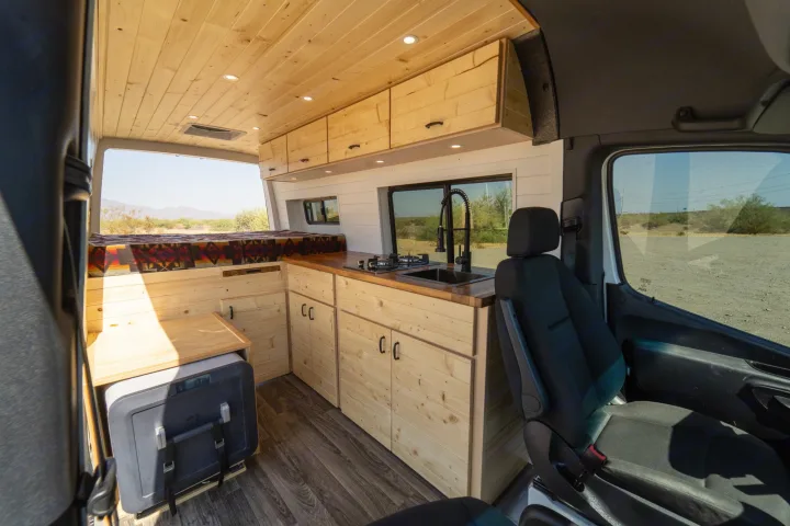 Spacious RV rental interior featuring a custom wooden build with kitchenette, comfortable bed, and portable fridge.. Mercedes-Benz Sprinter 2021