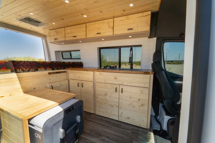 Spacious custom RV rental interior featuring a modern wood kitchen, comfy seating, and ample storage.. Mercedes-Benz Sprinter 2021