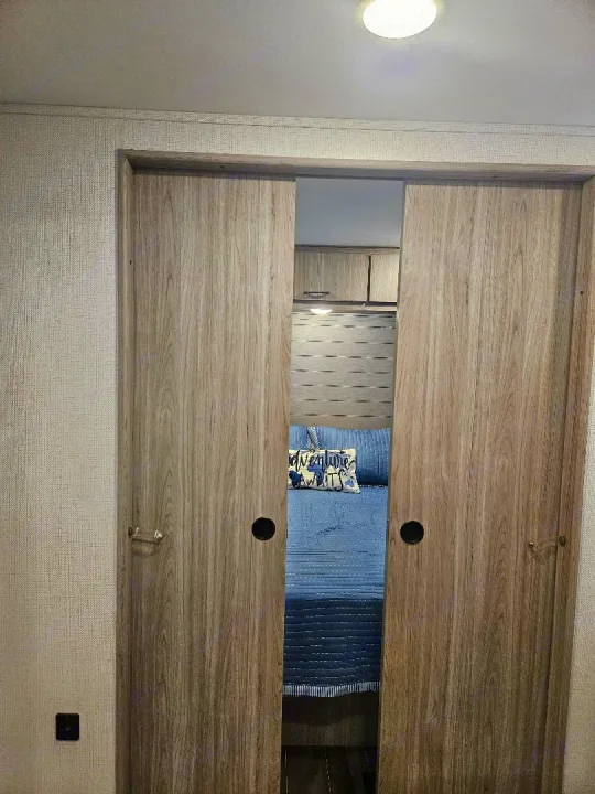 Discover the cozy bedroom inside an RV rental, partially visible through modern sliding doors, featuring blue bedding and an "Adventure Awaits" pillow.. Keystone RV Passport SL 2021
