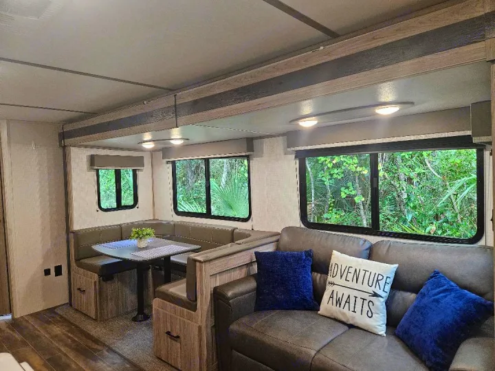 RV rental interior: Spacious living area with a booth dinette, sofa, and large windows revealing lush greenery.. Keystone RV Passport SL 2021