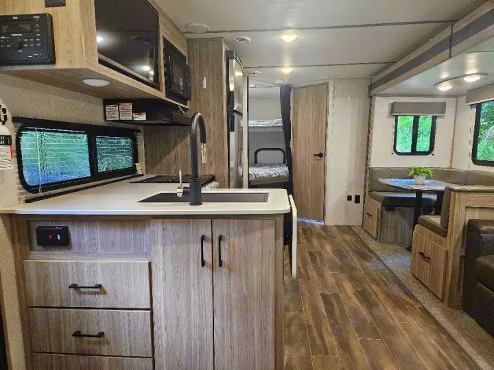 Spacious rv rental interior: kitchen with sink, dinette, and bunk beds in modern light wood tones.. Keystone RV Passport SL 2021