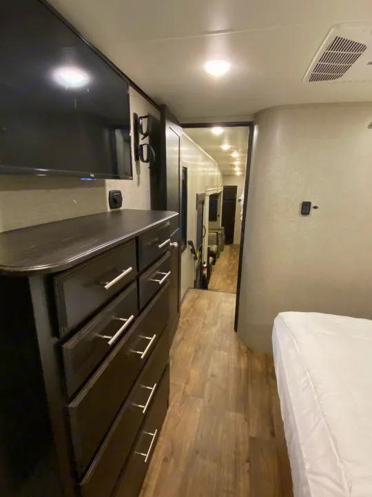 An RV rental's bedroom area with a dresser, TV, and an open hallway leading into the main living space. Clean and well-lit.. Jayco Eagle 2020
