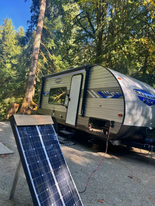 An rv rental, a travel trailer, is parked at a sunny forest campsite, using a portable solar panel for power.. Forest River Salem 2022
