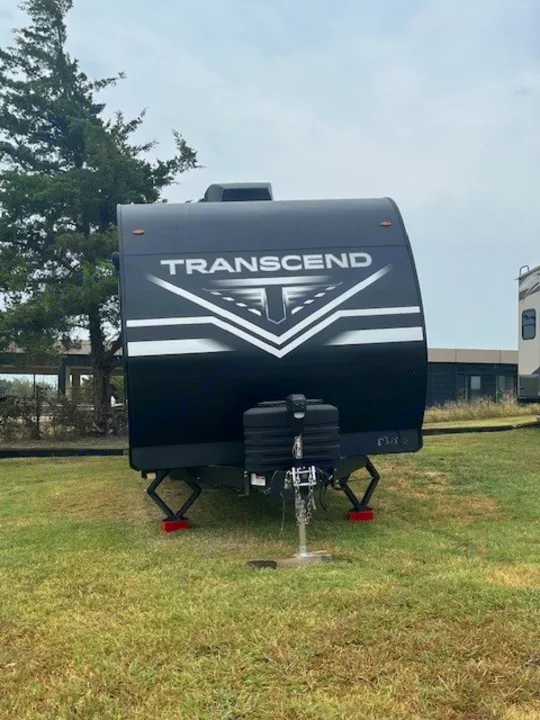 Black Transcend travel trailer, likely an RV rental, parked on grass with stabilizer jacks extended for stability.. Grand Design Transcend Xplor 2024
