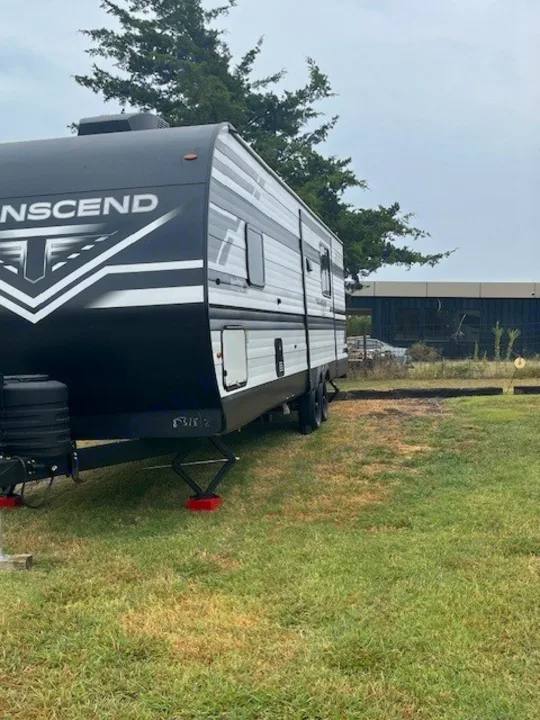 An RV rental, a black and white Transcend travel trailer, is parked on grass with stabilizing jacks.. Grand Design Transcend Xplor 2024