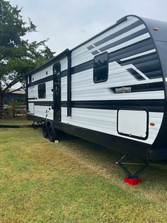 White & black Grand Design rv rental travel trailer on grass, awning extended. Perfect for outdoor trips.. Grand Design Transcend Xplor 2024