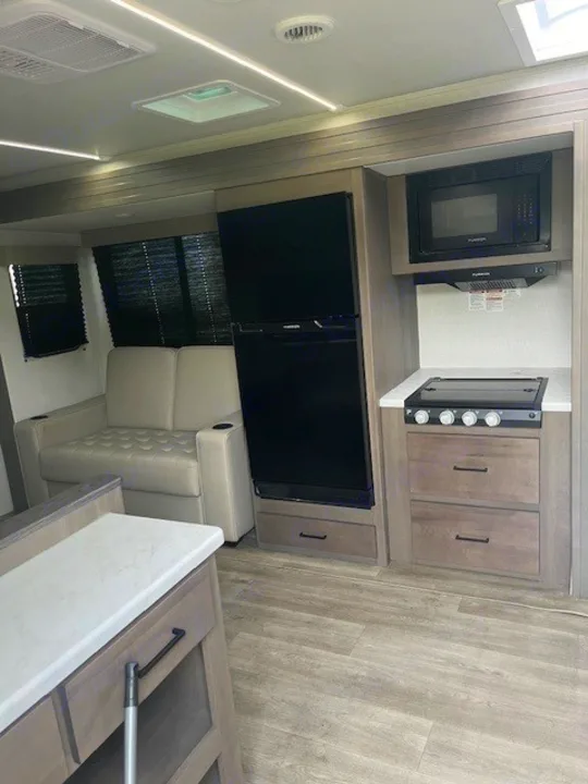 RV rental: Modern RV interior showcasing a compact kitchen with stovetop, microwave, and fridge, plus a comfortable living area sofa.. Grand Design Transcend Xplor 2024