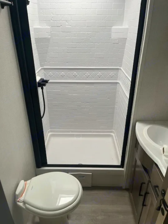 Clean RV rental bathroom with white shower, toilet, and sink. Features a compact, modern design ideal for travel comfort.. Grand Design Transcend Xplor 2024