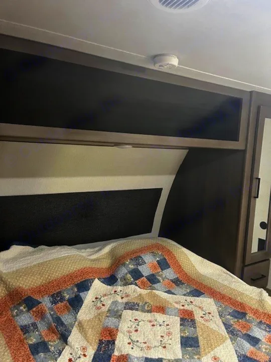 RV rental bedroom: patterned quilt, overhead storage, and ceiling smoke detector for travel safety.. Grand Design Transcend Xplor 2024