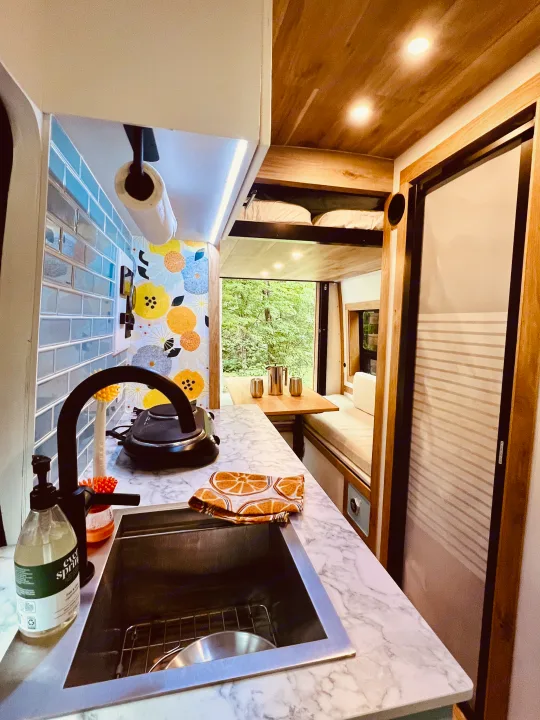 RV rental interior: stylish kitchen with marble counters, sink, and dining area with forest views.. Ford Transit 2023