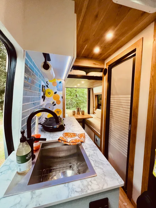 Compact RV rental interior featuring a kitchen sink, wood ceiling, dining area, and bunk beds.. Ford Transit 2023