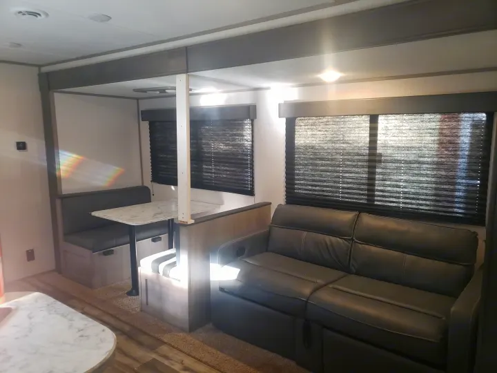 Modern RV rental living space featuring a cozy dinette, sofa, and bright windows. Ideal for travel.. Dutchmen Coleman Lantern LT 2022
