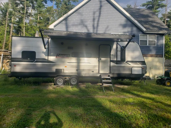 A spacious gray Coleman travel trailer, perfect for an RV rental, is parked with its awning extended beside a house.. Dutchmen Coleman Lantern LT 2022