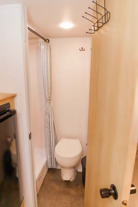 Compact RV rental bathroom with white toilet, striped shower curtain, and dark gray floor tiles.. Forest River Salem FSX 2023