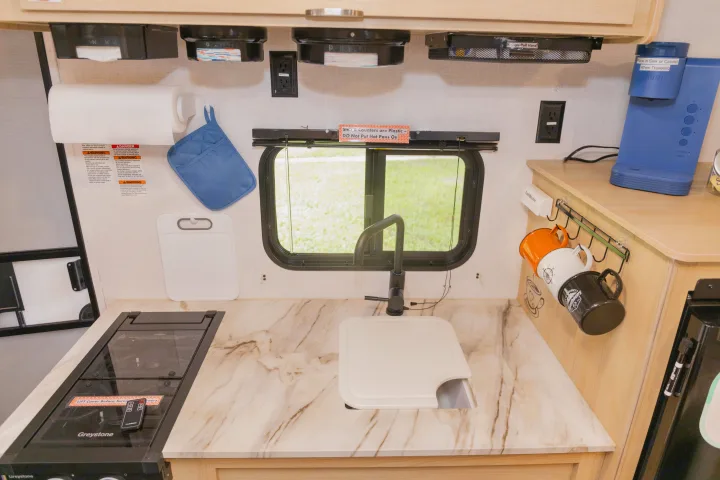 RV rental kitchen: compact counter with sink, stovetop, Keurig coffee maker, paper towels, and hanging mugs.. Forest River Salem FSX 2023