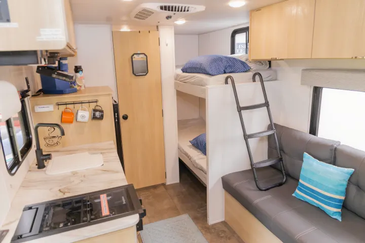 Inside a modern rv rental featuring a compact kitchen, bunk beds, and a cozy sofa area, ideal for family travel.. Forest River Salem FSX 2023