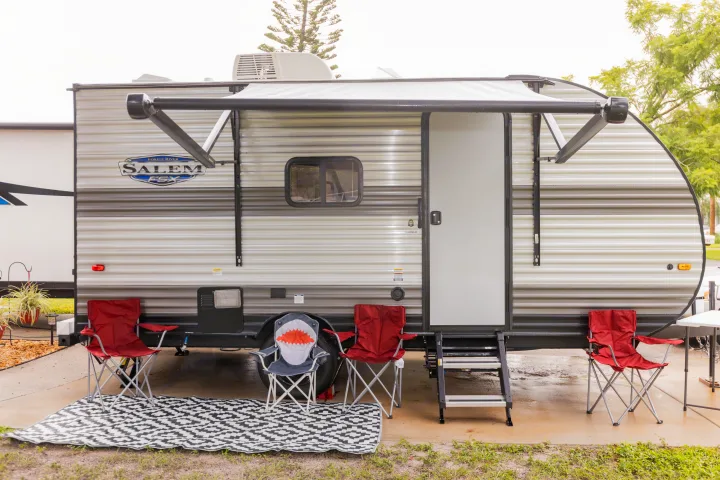 This RV rental at a campsite features an extended awning, outdoor rug, and camping chairs, ready for relaxation.. Forest River Salem FSX 2023