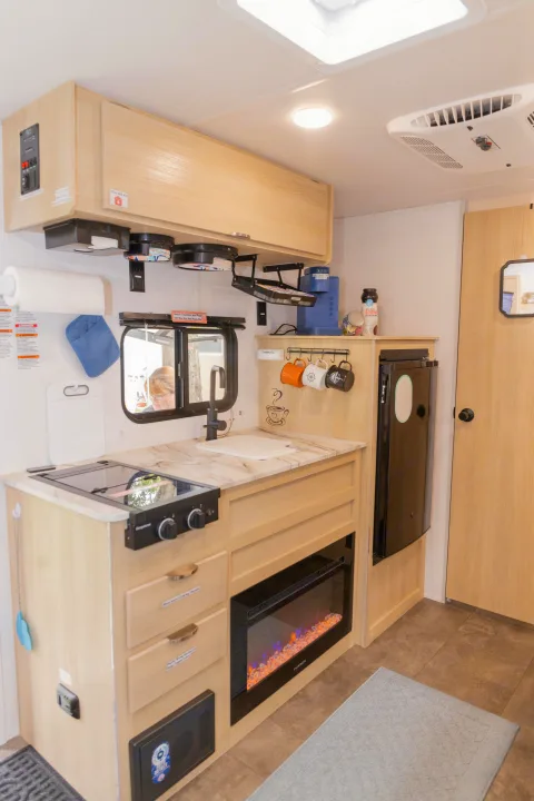 This RV rental kitchen features a compact stove, sink, electric fireplace, and ample storage, perfect for travel.. Forest River Salem FSX 2023