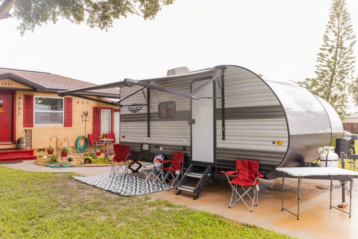 This RV rental travel trailer is parked next to a house, with an extended awning, camping chairs, and a folding table set up outside.. Forest River Salem FSX 2023