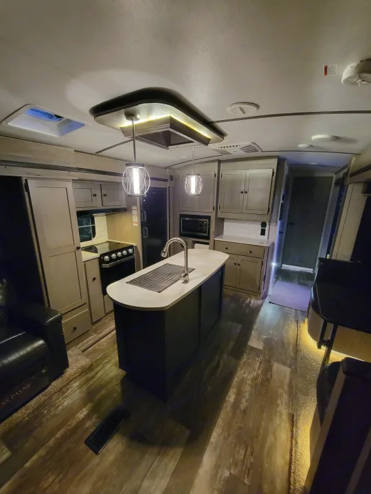 Step inside this modern RV rental! Features a well-equipped kitchen island, comfortable living space, and warm lighting.. Keystone RV Outback 2019