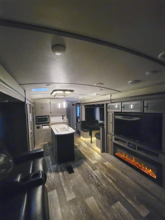 Spacious RV rental interior with kitchen island, dining booth, and cozy living area featuring a TV and electric fireplace.. Keystone RV Outback 2019