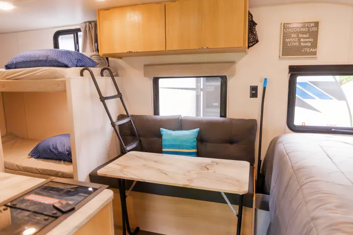 Cozy rv rental interior with bunk beds, a dinette table, kitchen counter, and main bed. Perfect for family adventures.. Forest River Salem FSX 2023
