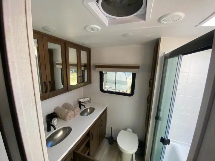 Spacious RV rental bathroom featuring a double vanity, sleek shower, & toilet. Enjoy residential comfort on your travels.. Forest River Rockwood Signature 2024