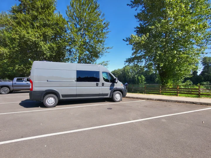 Grey camper van RV rental parked by a river, ready for your next travel adventure.. Custom Ram Promaster 2023
