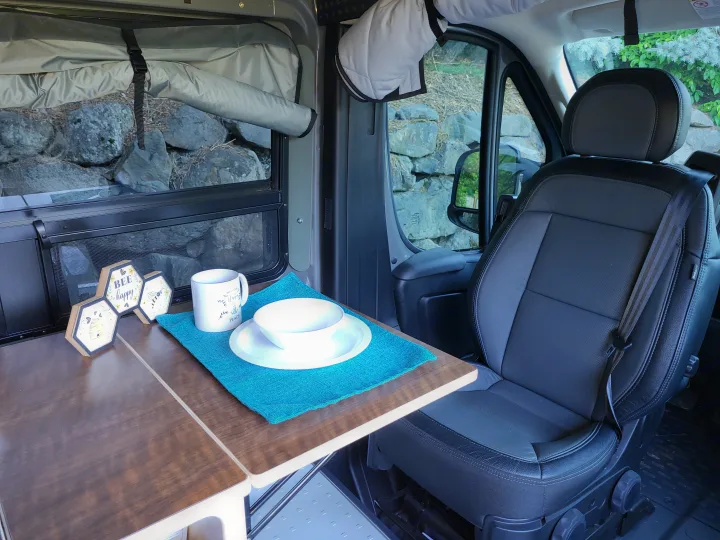 Cozy camper van rv rental interior: dining table set with plate/mug & scenic outdoor view.. Custom Ram Promaster 2023