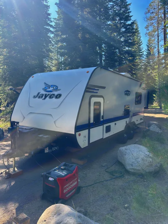 A Jayco travel trailer is set up at a forest campsite with a Predator generator, hinting at an RV rental adventure.. Jayco Jay Flight 2018