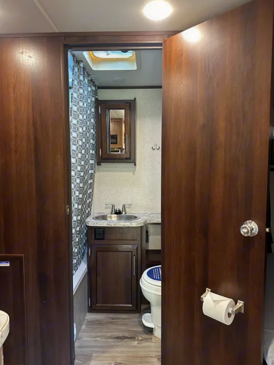 RV rental bathroom. This compact space features a dark wood vanity, sink, mirrored medicine cabinet, and patterned shower curtain.. Jayco Jay Flight 2018