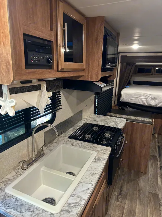 Clean RV rental interior featuring a kitchen with dual sink, stove, microwave, and entertainment system. Bedroom in back.. Jayco Jay Flight 2018