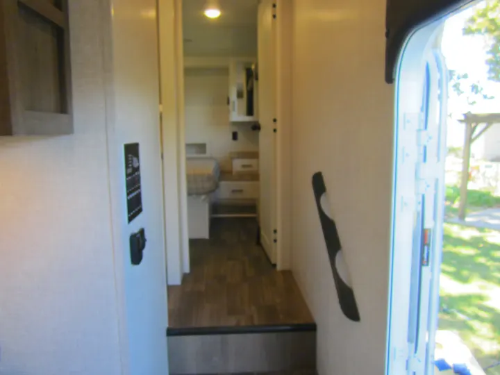 Step into this RV rental, featuring a hallway leading to the bedroom, a control panel, and an open door to the bright outdoors.. Jayco Eagle HT 2024