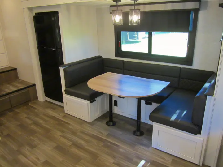 This inviting RV rental interior features a cozy black dinette booth with a light table, refrigerator, and window with blinds.. Jayco Eagle HT 2024